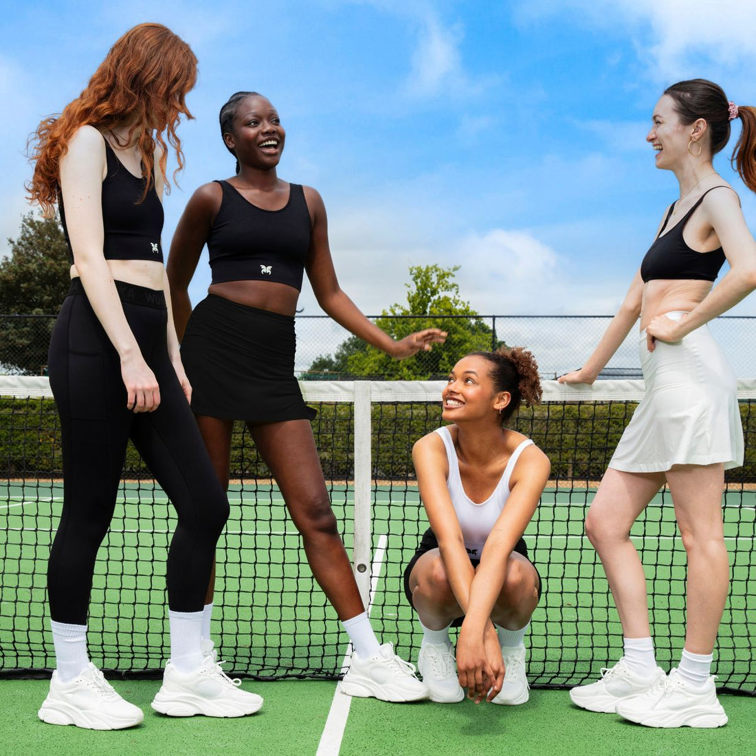 four girls stand by a tennis net laughing and enjoying the sunshine 